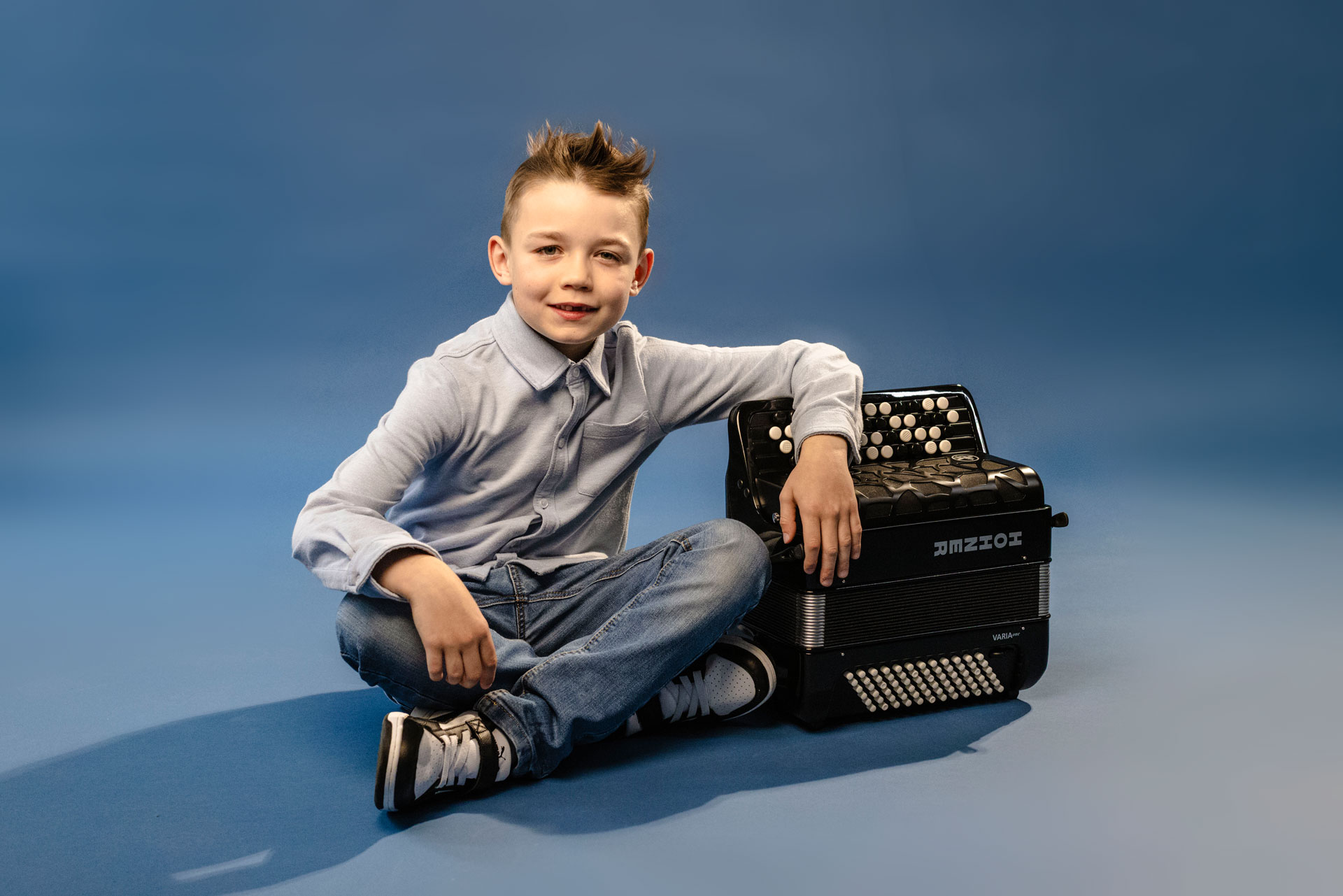 young boy, brown hair, sitting next to a HOHNER accordion