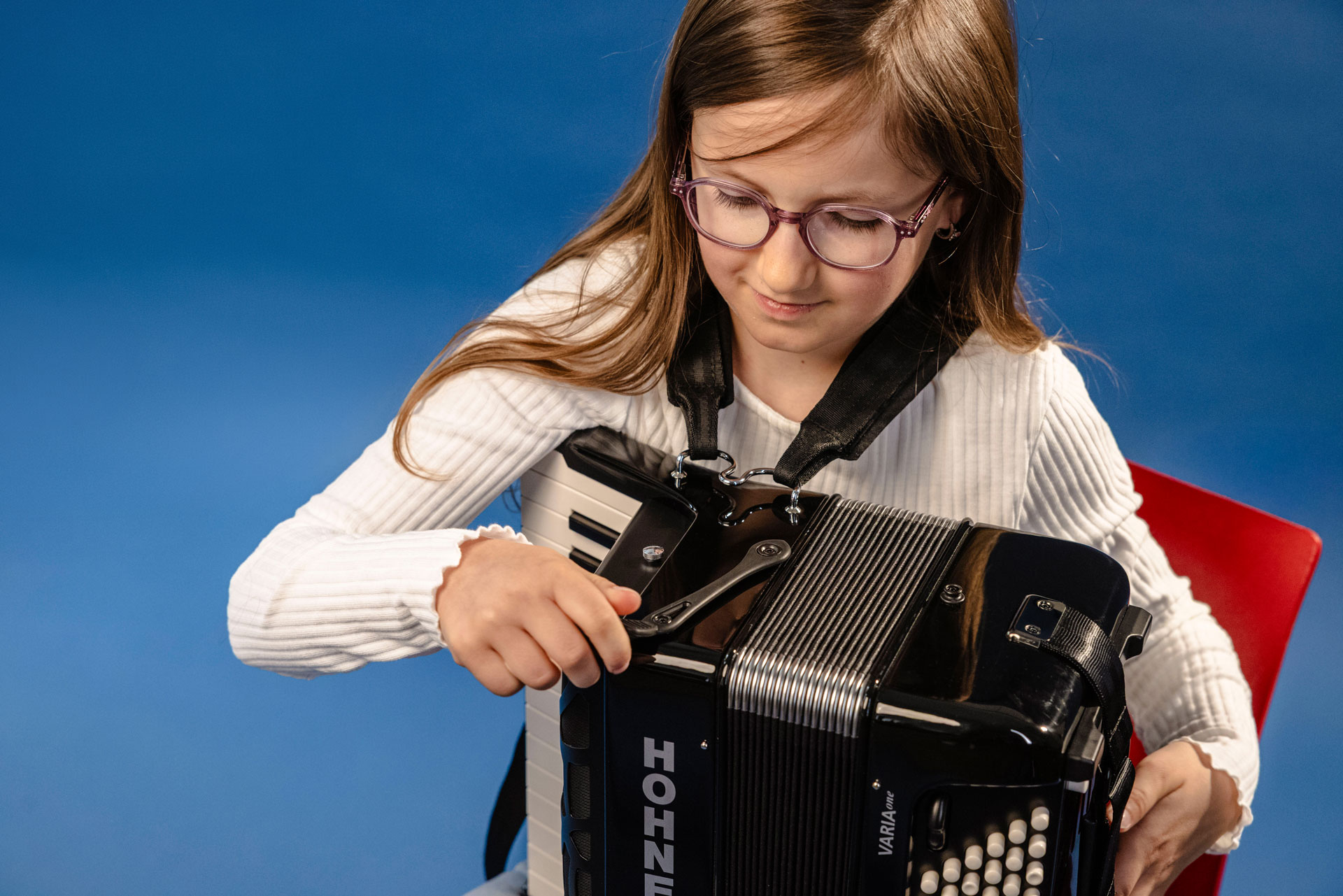 young girl, brown hair, and glasses playing HOHNER accordion